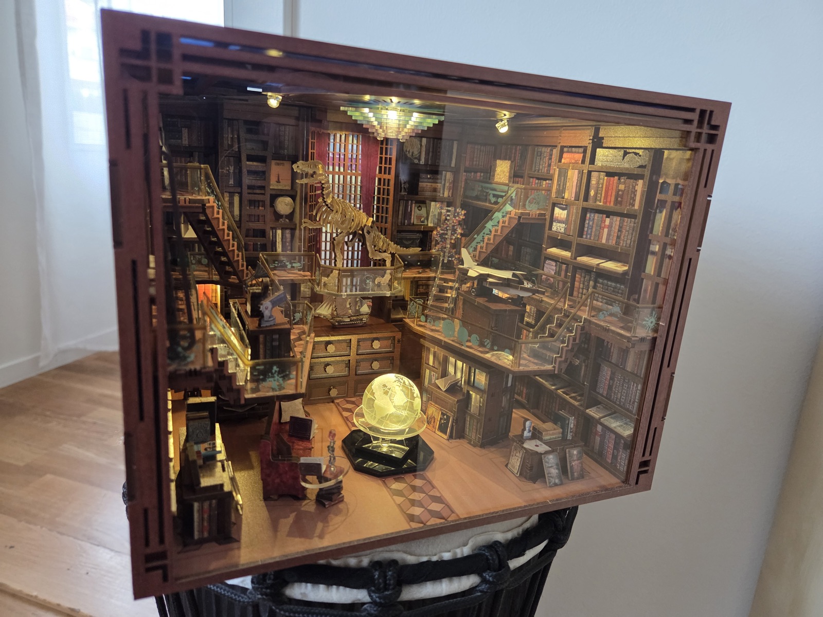 Miniature library room box with a dinosaur skeleton, staircases, floor-to-ceiling bookshelves and a glowing globe